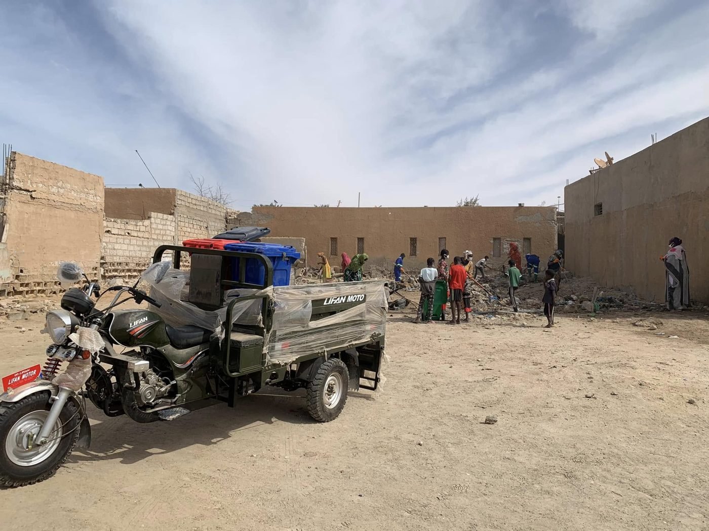 Tricycle de collecte et bacs à déchets, avec des habitants qui nettoient un terrain à Sebkha